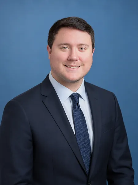 William Chase Roberts, P.E., in a navy suit and tie against a blue background.